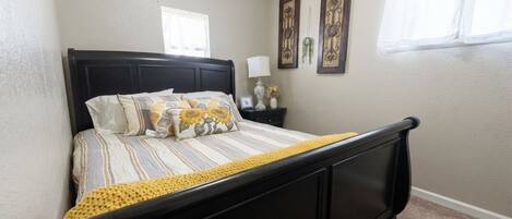 A bedroom with a bed, a nightstand, a lamp, and two wall-mounted picture frames.
