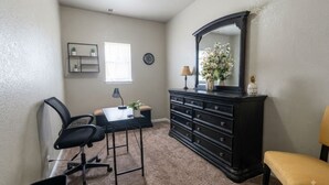 Una habitación con escritorio, silla, cómoda, espejo y una pequeña estantería con plantas.