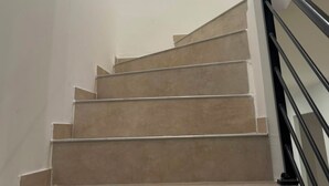 Eine Treppe mit beigen Stufen und einem schwarzen Geländer, die in einem modernen Innenraum nach oben führt.