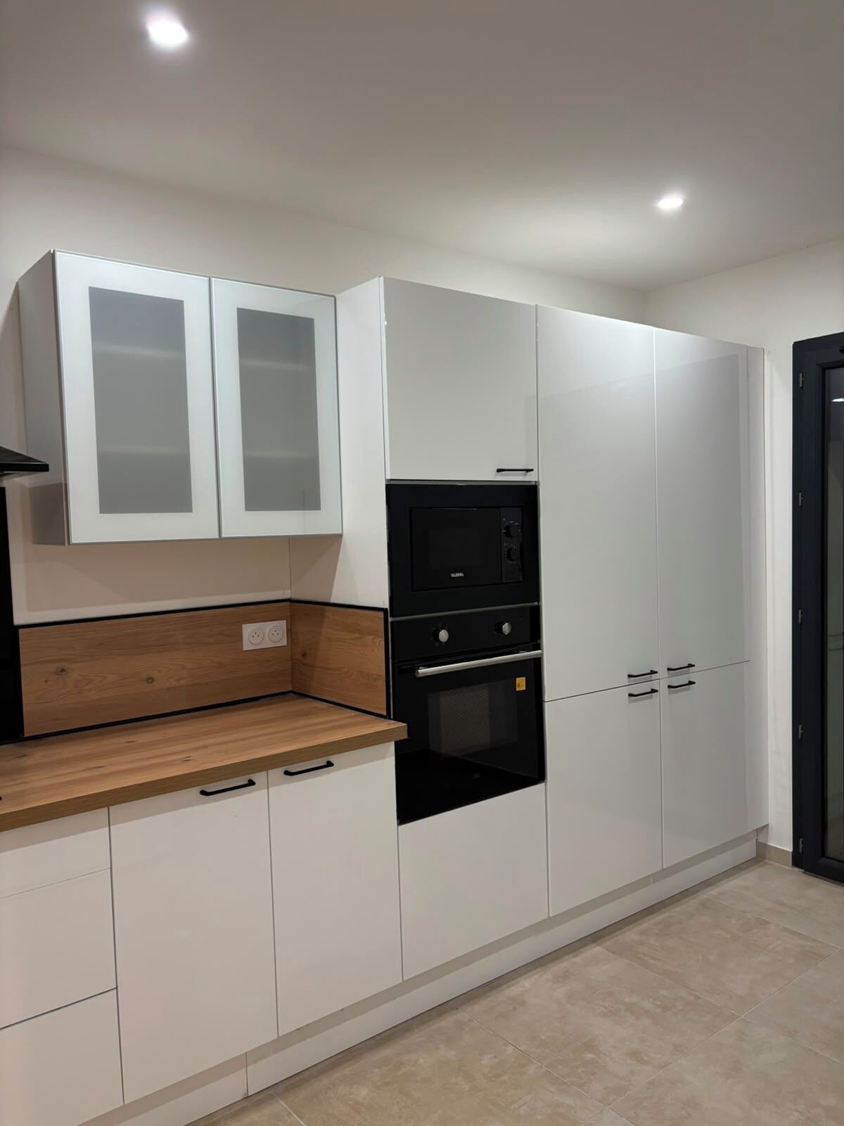 Une cuisine moderne avec des meubles blancs, un four noir et un plan de travail en bois.
