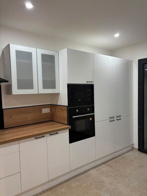 A modern kitchen with white cabinets, a black oven, and a wooden countertop. - Modern Villa with Private Pool in Vias – Your Perfect South of France Getaway ☀️ (Vias)