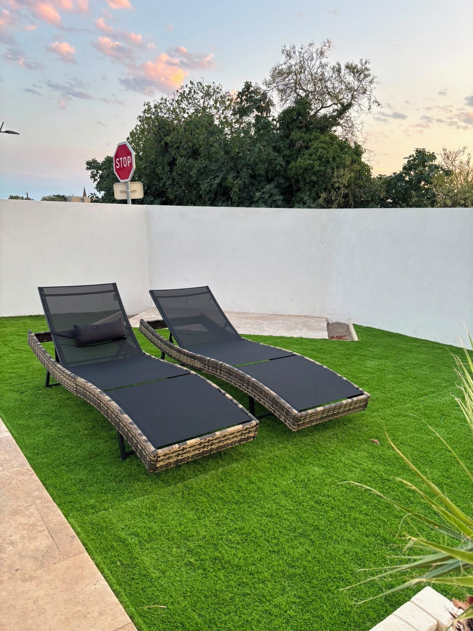 Deux fauteuils de jardin sont placés sur une pelouse artificielle, avec un panneau de signalisation et des arbres en arrière-plan.