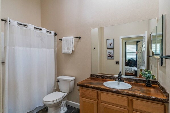 A bathroom with a shower curtain, toilet, sink, and a large mirror. - TPC Golf Condo/Patio/Golf Course View/Sleeps 8/Community Pool/Hot Tub (Scottsdale)