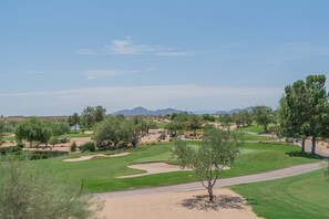 Ein Golfplatz mit blauem Himmel, grünem Rasen, Bäumen und einem Berg im Hintergrund.