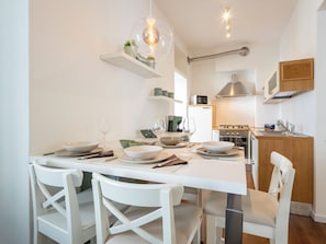 A modern kitchen with white cabinetry, a dining table set with plates, bowls, and cutlery, and a hanging light fixture. - Genzianella Alpine Apartment by Interhome (Chiavenna)