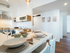 Une cuisine moderne avec un coin repas, des meubles blancs et un îlot central agrémenté de bols et de verres à vin.