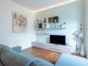 A modern living room with a flat-screen TV, light wood flooring, a blue sofa, and a minimalist shelving unit. - Genzianella Alpine Apartment by Interhome (Chiavenna)