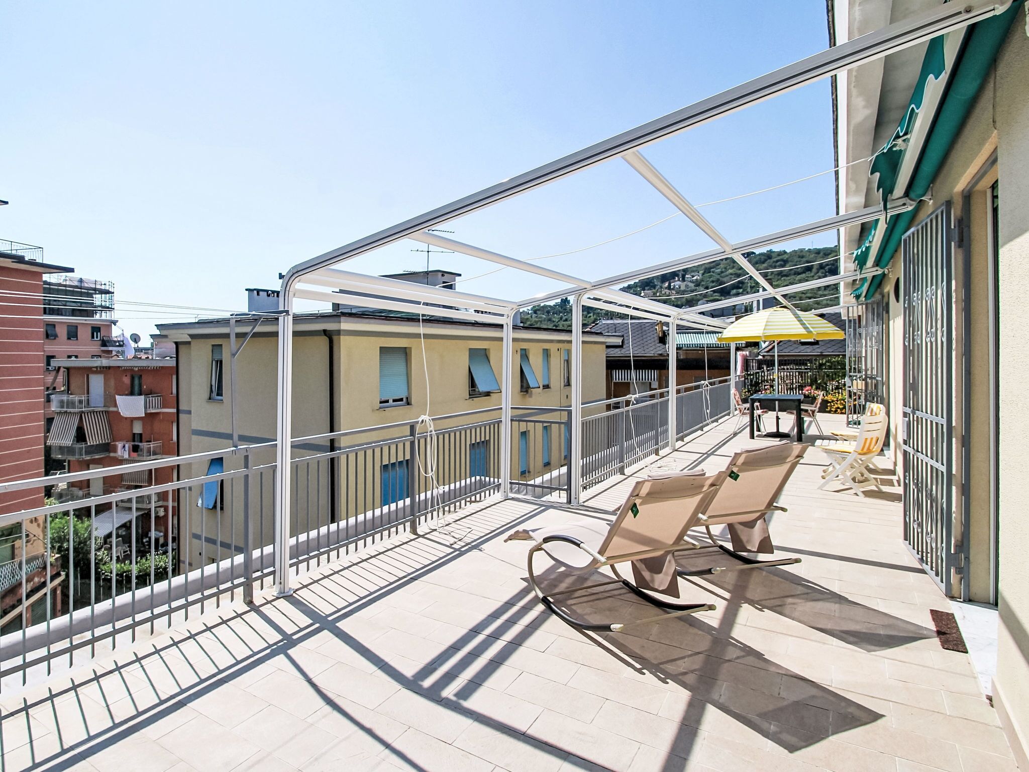 A balcony with a glass enclosure, two lounge chairs, and a yellow umbrella.
