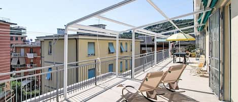 A balcony with a glass enclosure, two lounge chairs, and a yellow umbrella.
