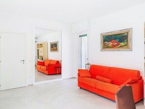 A modern living room with a bright orange sofa, a framed painting, and a door leading to another room. - Attico Alda by Interhome (Rapallo)