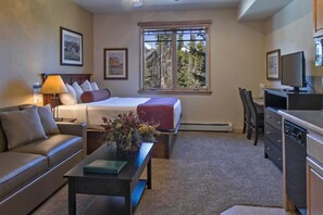 A hotel room with a bed, a sofa, a desk, a television, and a window with a view of trees. - Delightful studio in Breckenridge winter wonderland -mountain/ski getaway (Breckenridge)