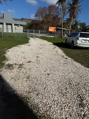 A gravel path leading to a building with a fenced area and a parked car.