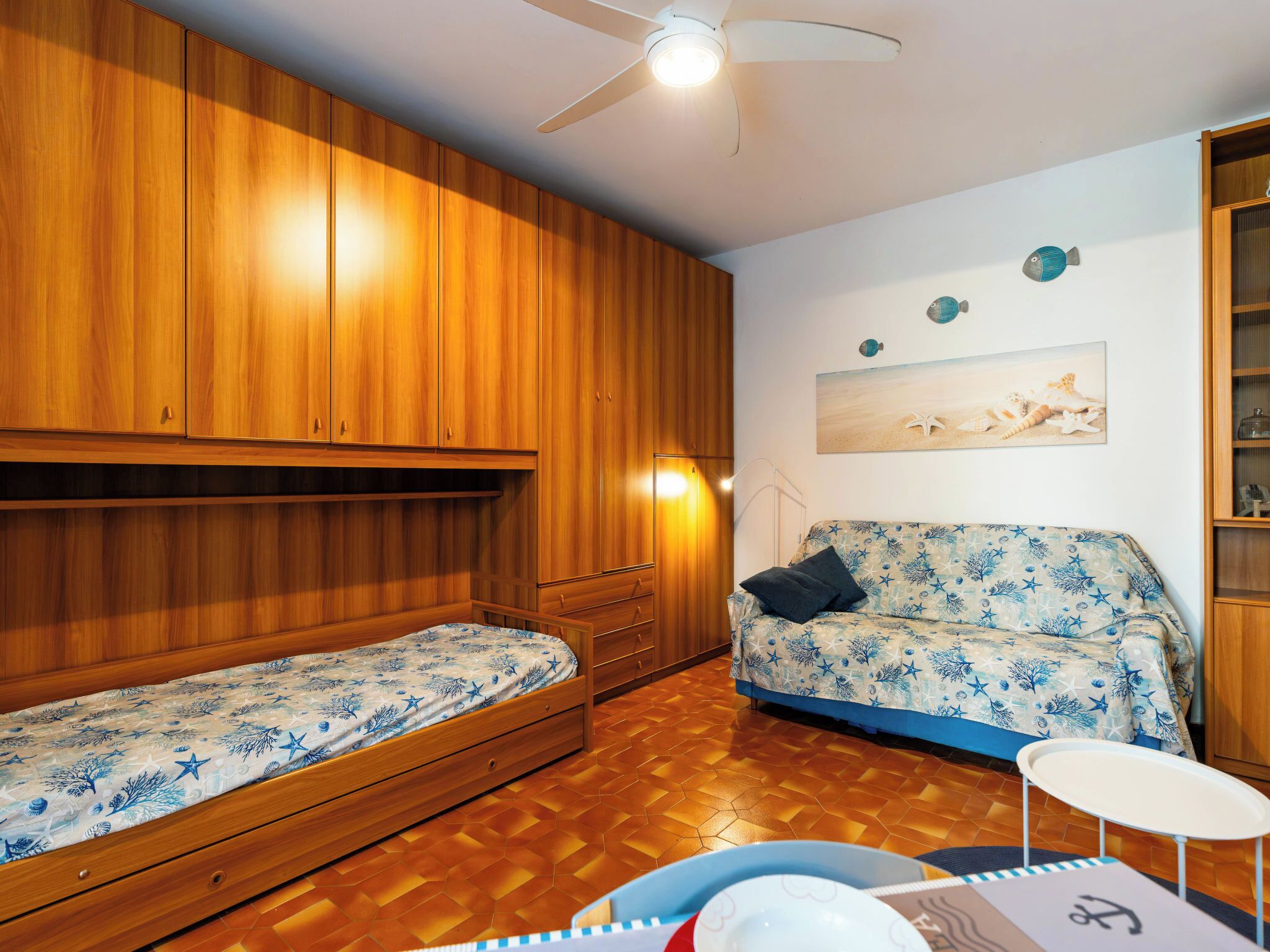 A room with two single beds, a sofa, a ceiling fan, and a wall with decorative items.