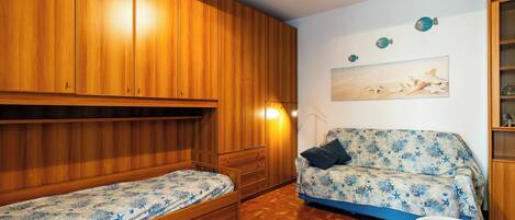 A room with two single beds, a sofa, a ceiling fan, and a wall with decorative items.