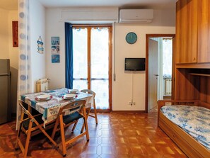 Una habitación con una mesa de comedor lista para dos personas, una cama con colcha estampada, un televisor montado en la pared y un armario de madera.