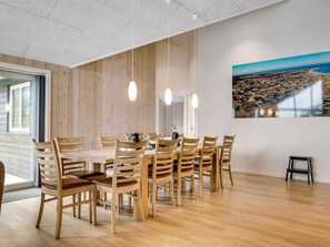 Un comedor con mesa y sillas de madera, iluminación colgante y un cuadro de un paisaje urbano en la pared.