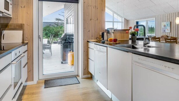 A modern kitchen with wooden paneling, a built-in dishwasher, and a view to the outdoor patio. - "Arsi" - 350m from the sea by Interhome (Thisted)