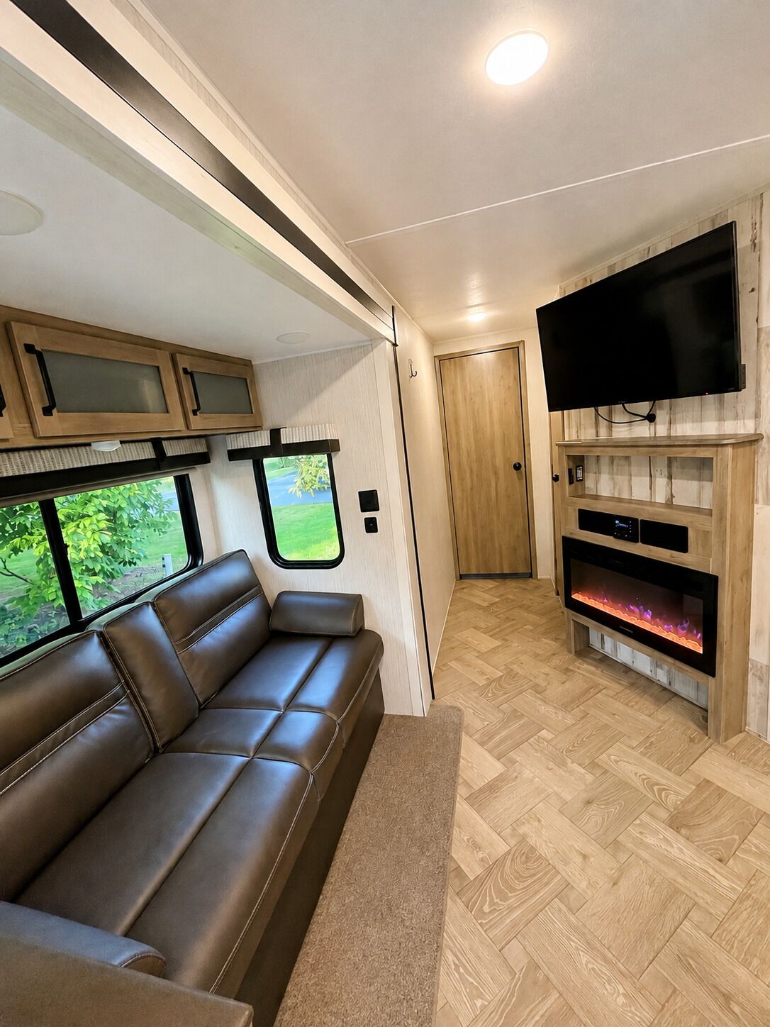 Un intérieur de camping-car chaleureux, avec un canapé en cuir, un téléviseur à écran plat fixé à un mur en bois et une cheminée.