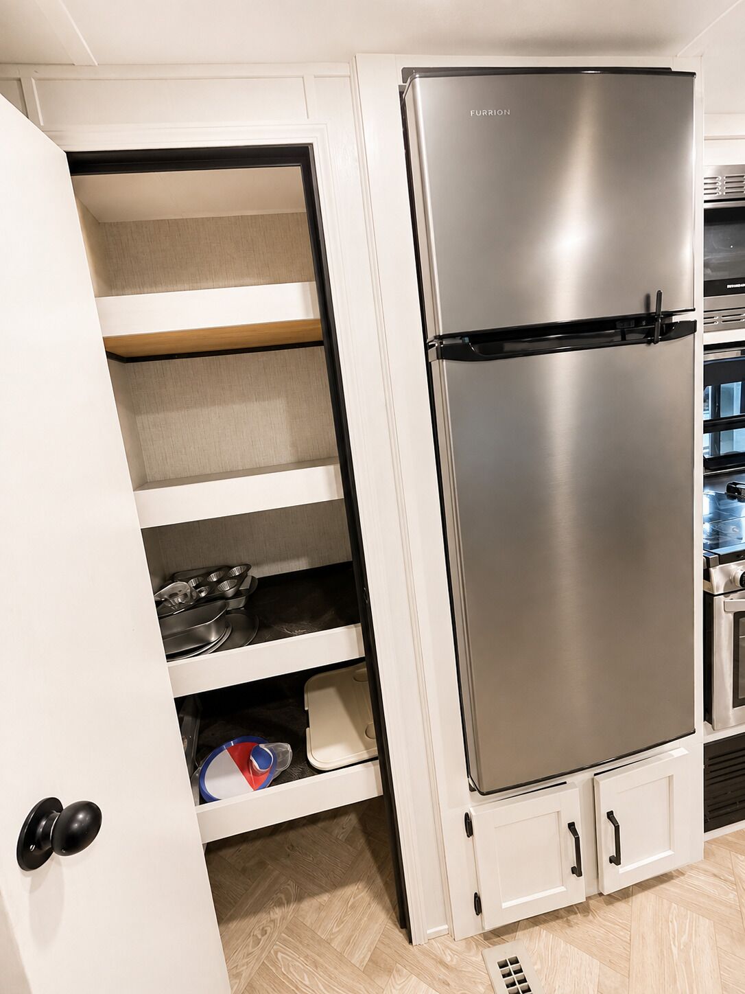 A modern kitchen with a stainless steel Furrion refrigerator, white cabinetry, and a herringbone-patterned floor.