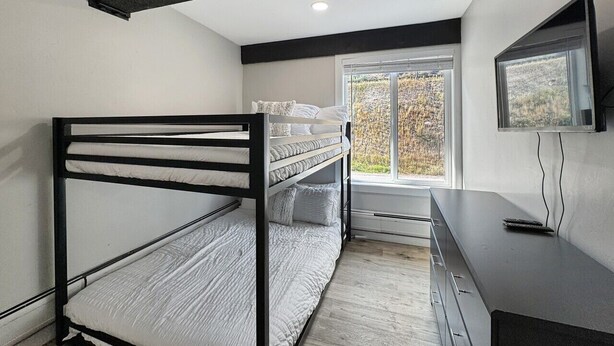 Een stapelbed met bureau en televisie in een kamer met raam.
