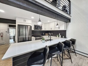 A modern kitchen with a large island, stainless steel appliances, pendant lighting, and black bar stools. - Family-Friendly 3BR Vail Condo near Gore Creek, Steps to Free Bus, 2 Parking Spaces (Vail)