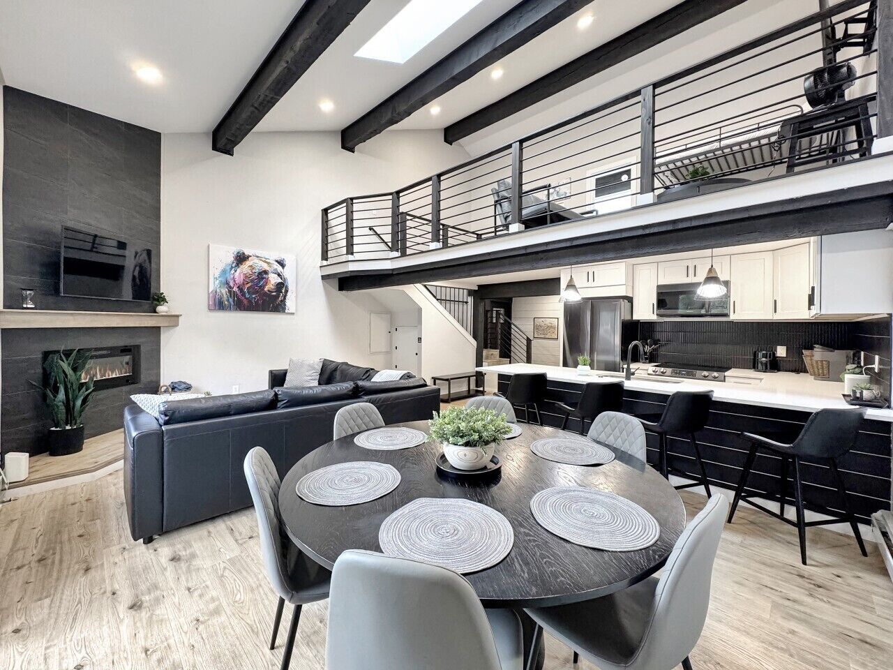 A modern kitchen with a central island, a dining area with a round table, and a living room with a sofa and fireplace.
