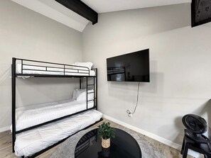 Ein Etagenbett mit an der Wand montiertem Flachbildfernseher, ein kleiner runder Tisch mit einer Pflanze und ein Stuhl.