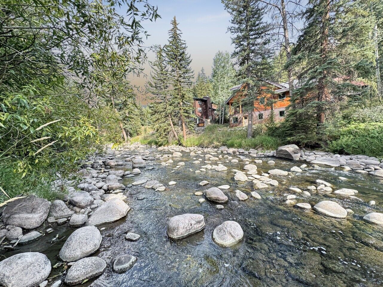 A river with rocks and trees, surrounded by a cabin with a red roof.