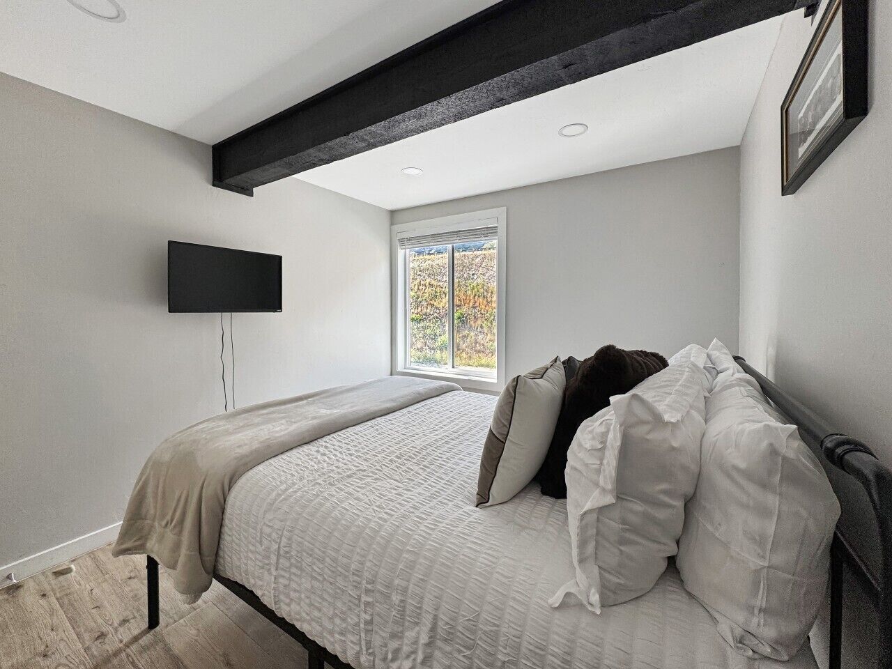 Quarto com cama, televisão de tela plana na parede e janela com vista para árvores.