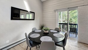 Een eetruimte met een ronde tafel, zes stoelen, een plant in het midden en uitzicht op het buitenleven via een schuifdeur.