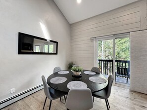 A dining area with a round table, six chairs, a central plant, and a view of the outdoors through a sliding glass door. - Family-Friendly 3BR Vail Condo near Gore Creek, Steps to Free Bus, 2 Parking Spaces (Vail)