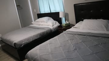A hotel room with two single beds, a bedside table with a lamp, and a door leading to a hallway.