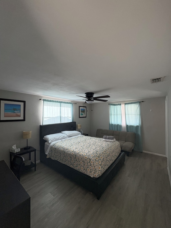 A bedroom with a bed, a ceiling fan, a nightstand, a lamp, and a window with curtains.