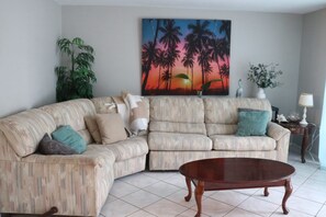 A living room with a sectional sofa, a coffee table, and a painting of palm trees.