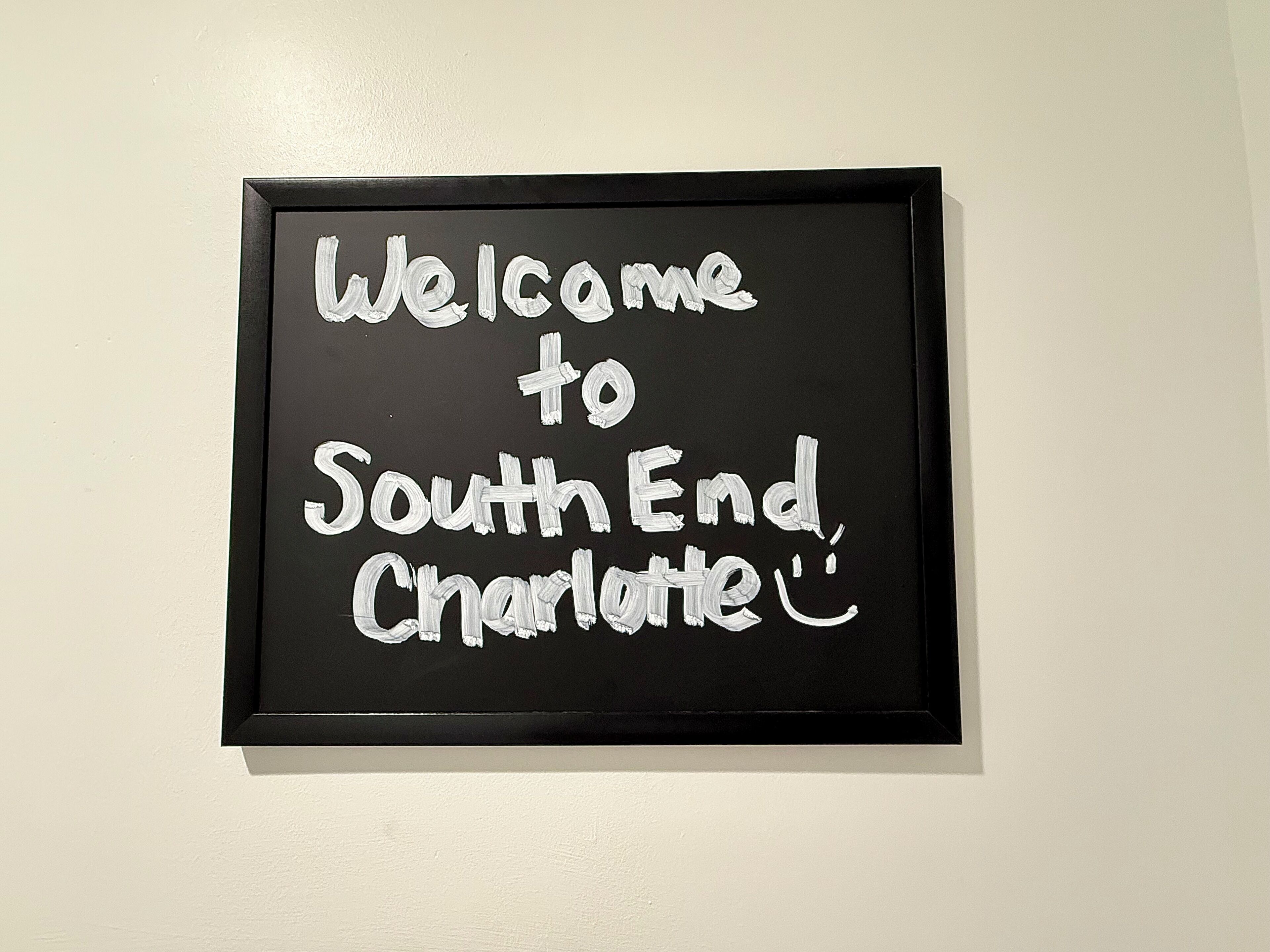 A framed welcome sign with the text 'Welcome to South End Charlotte' on a white wall.