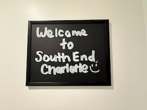 A framed welcome sign with the text 'Welcome to South End Charlotte' on a white wall. - The Golden European Flat (Charlotte)