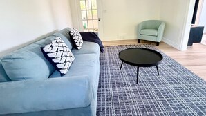 A living room with a light blue sofa, two patterned pillows, a black coffee table, and a patterned rug.
