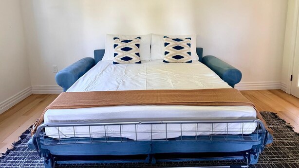 A bed with a white mattress, two pillows with a geometric pattern, and a blue headboard.
