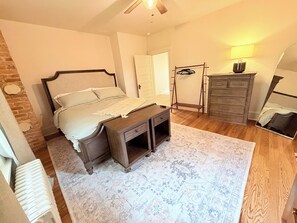 Ein Schlafzimmer mit Bett, Kommode, Spiegel und einer Kleiderstange.