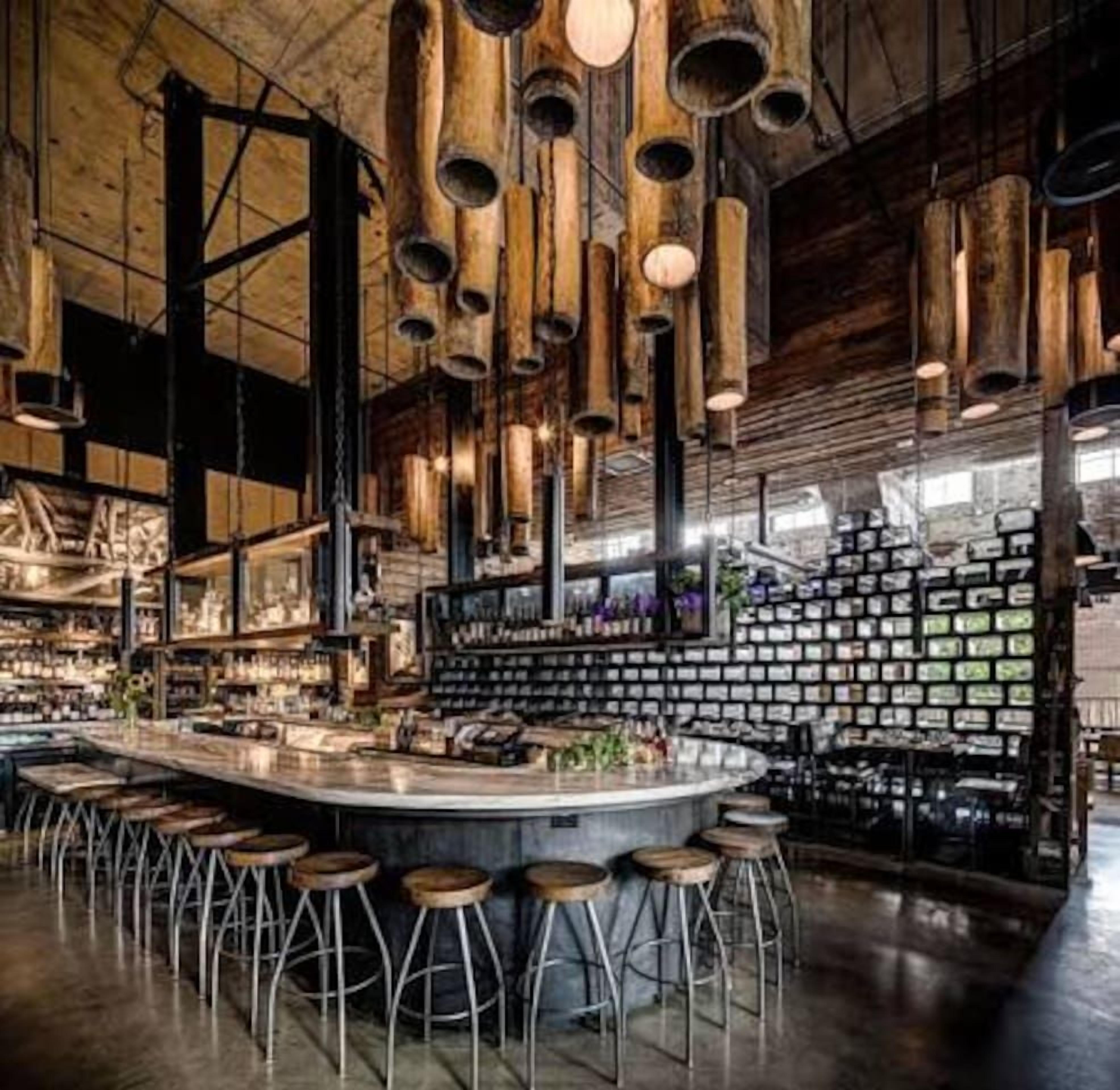 Un bar con una barra central y taburetes, vigas de madera y lámparas colgantes.
