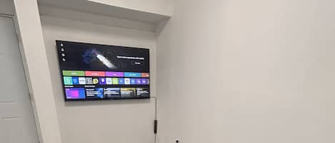 A modern living room with a grey sofa, a glass coffee table, and a flat-screen TV mounted on the wall displaying various apps.