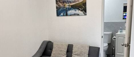 A modern living room with a gray sofa, a glass coffee table, and a painting of a mountain landscape on the wall.