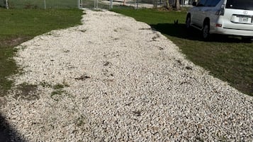 Un chemin de gravier mène à un bâtiment doté d’une zone délimitée par une clôture et où est garée une voiture.