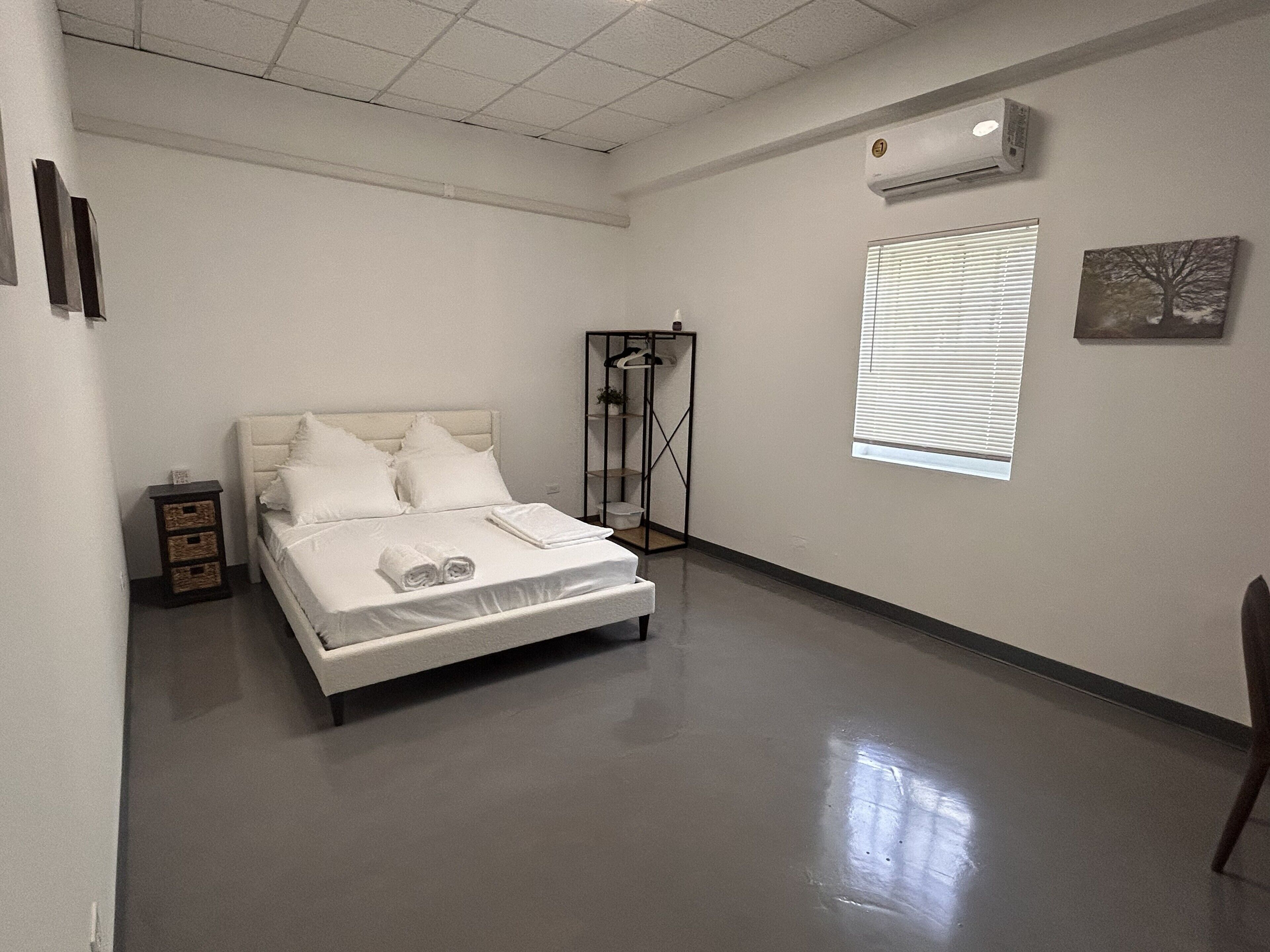 A hotel room with a bed, a wardrobe, a window with blinds, and an air conditioning unit.