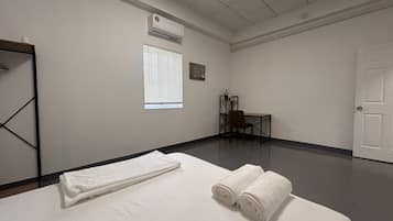 Habitación de hotel con cama, una silla, un escritorio, ventana con persianas y aire acondicionado.