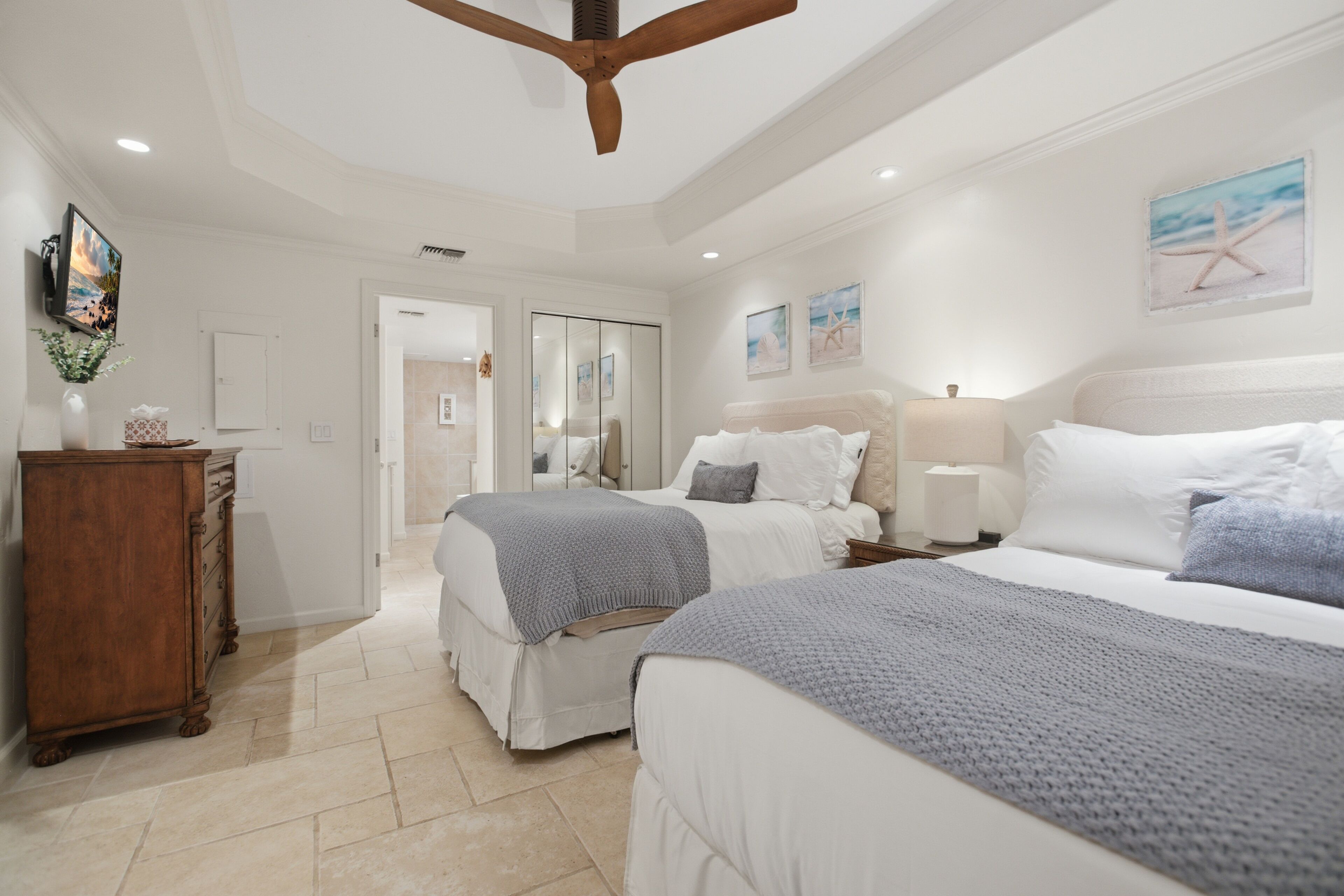 A bedroom with two beds, a wooden wardrobe, a bedside table with a lamp, and a painting on the wall.