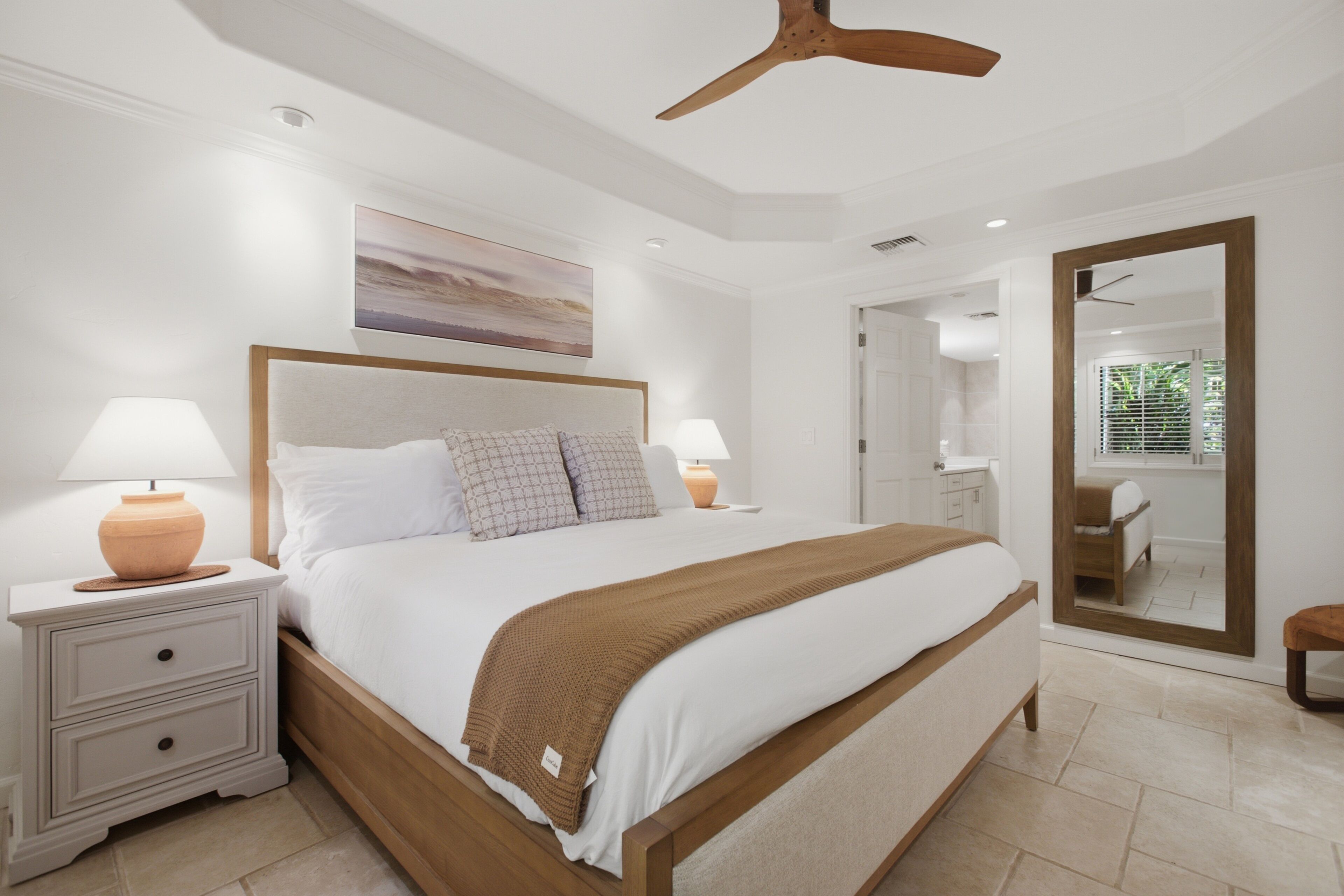 A bedroom with a bed, bedside tables, a ceiling fan, a painting, and a mirror.