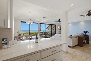A modern kitchen with a large island, dining area with chairs, and a view of the ocean. - Newly Remodeled/Refurnished Oceanfront Makena Surf Condo - Ground Floor (Kihei)