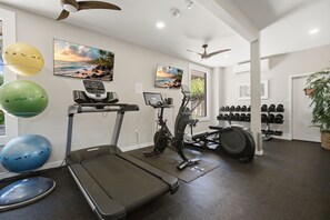 Ein Fitnessstudio mit Trainingsgeräten, darunter Laufbänder, Ergometer und einem an der Wand montierten Fernseher.
