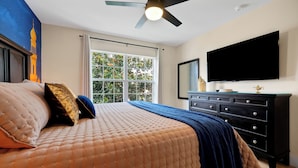 Ein Schlafzimmer mit Bett, Deckenventilator, Fenster und Fernseher.
